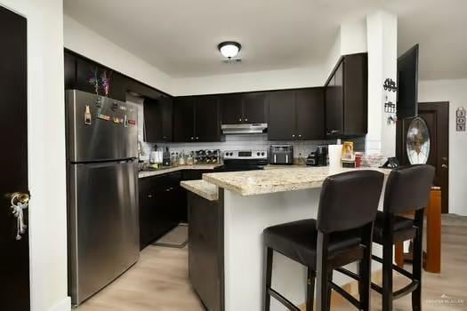 kitchen with a breakfast bar, light wood-type flooring, light stone countertops, kitchen peninsula, and stainless steel appliances