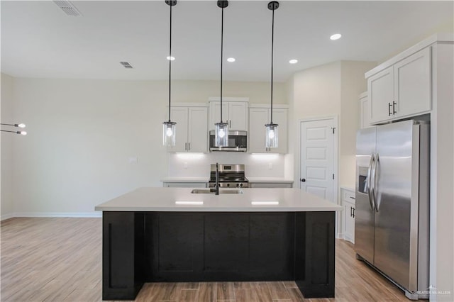 kitchen featuring white cabinetry, decorative light fixtures, stainless steel appliances, and a center island with sink