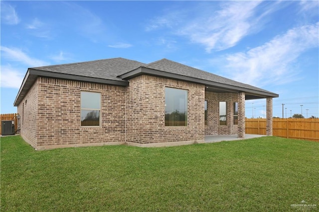 rear view of house with central AC unit, a lawn, and a patio