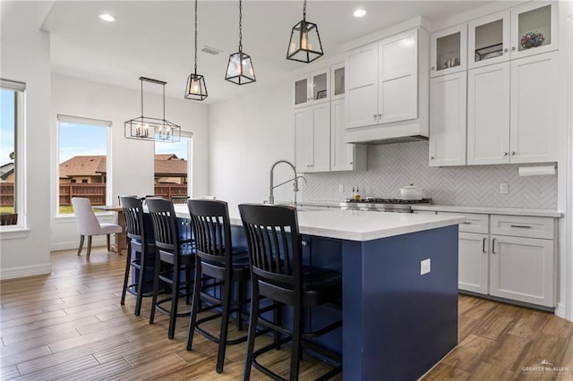 1405 Jocelyn Cir, Harlingen, TX 78552 - kitchen featuring light countertops, wood finished floors, a kitchen island with sink, and backsplash