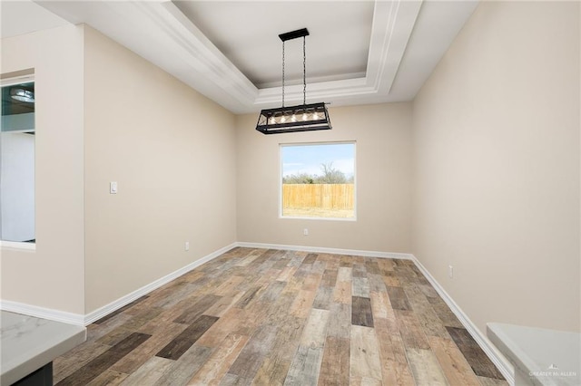 unfurnished dining area featuring a tray ceiling, light wood-type flooring, and baseboards