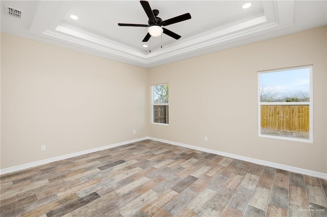 empty room with light wood-type flooring, a raised ceiling, visible vents, and baseboards