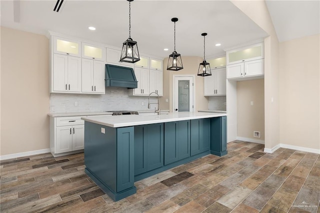 kitchen featuring tasteful backsplash, white cabinets, custom range hood, and a sink