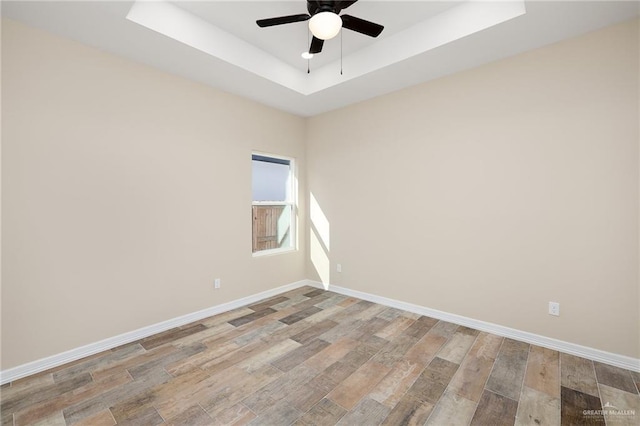 unfurnished room with ceiling fan, a tray ceiling, light wood-style flooring, and baseboards