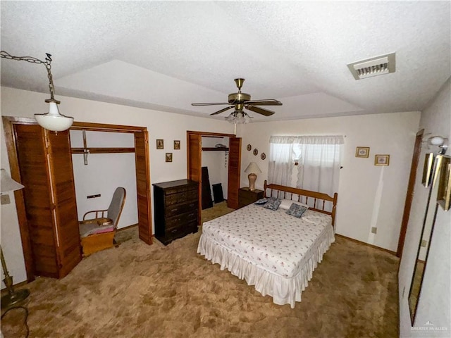 carpeted bedroom with ceiling fan, vaulted ceiling, two closets, and a textured ceiling