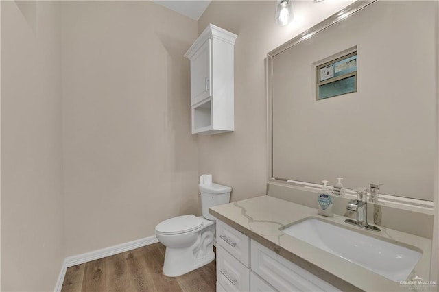 half bath with toilet, wood finished floors, vanity, and baseboards