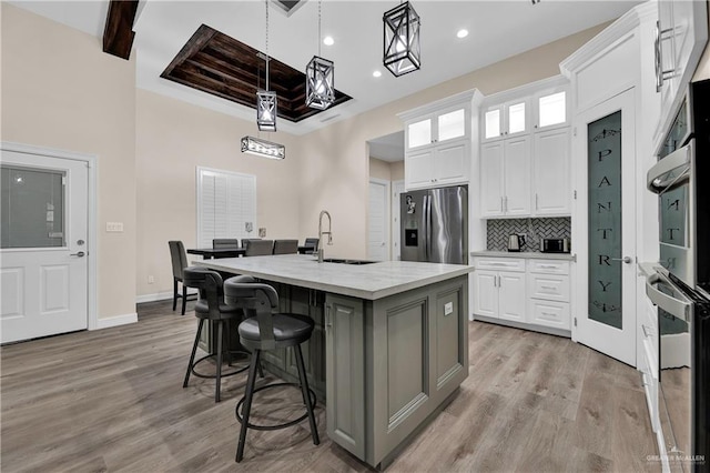 kitchen with decorative backsplash, light wood-style flooring, a kitchen island with sink, white cabinetry, and stainless steel refrigerator with ice dispenser