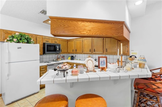 kitchen featuring white appliances, a kitchen bar, tile counters, and kitchen peninsula