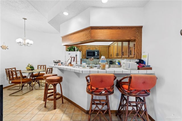 kitchen featuring hanging light fixtures, black microwave, tile counters, a kitchen breakfast bar, and white fridge