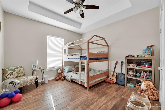 bedroom featuring a ceiling fan, a raised ceiling, wood finished floors, and baseboards