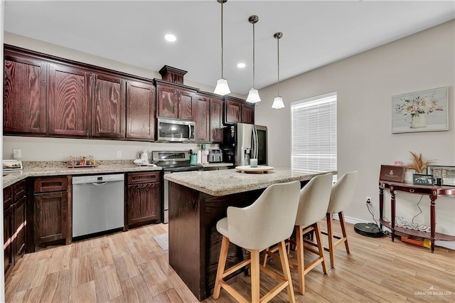 kitchen featuring light wood finished floors, appliances with stainless steel finishes, a kitchen breakfast bar, decorative light fixtures, and a center island