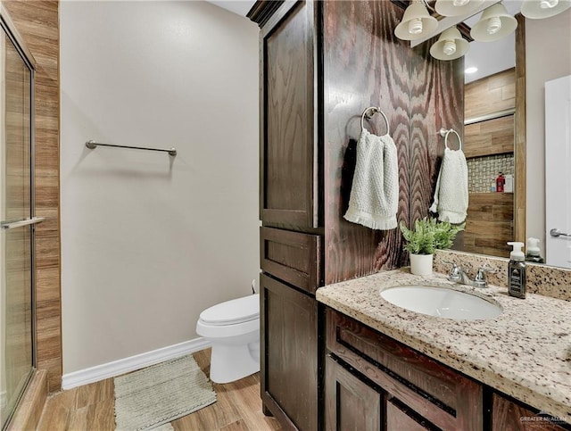 full bath featuring toilet, wood finished floors, a tile shower, baseboards, and vanity