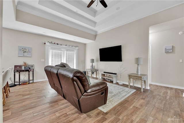 living room featuring a raised ceiling, light wood-style flooring, baseboards, and ceiling fan