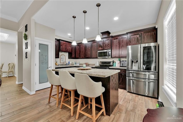 kitchen featuring pendant lighting, a breakfast bar, light wood-style flooring, a center island, and stainless steel appliances