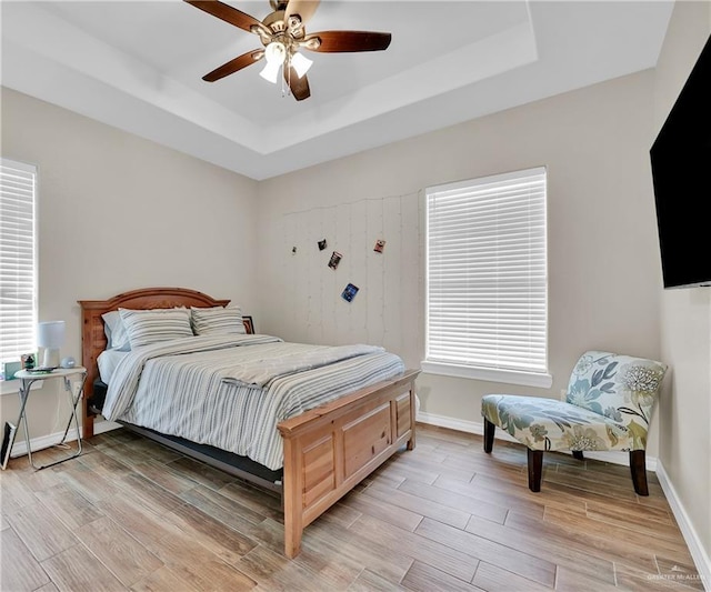 bedroom featuring a tray ceiling, baseboards, light wood-type flooring, and ceiling fan