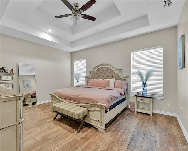 bedroom with visible vents, baseboards, ceiling fan, light wood-style flooring, and a raised ceiling