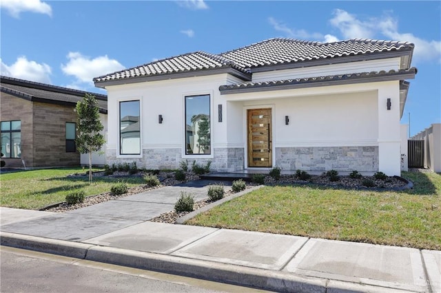 mediterranean / spanish house with stone siding, a tiled roof, a front lawn, and stucco siding