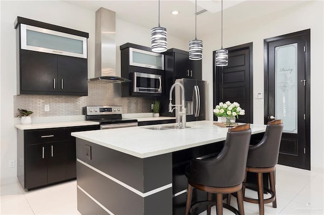 kitchen featuring pendant lighting, sink, appliances with stainless steel finishes, an island with sink, and wall chimney exhaust hood