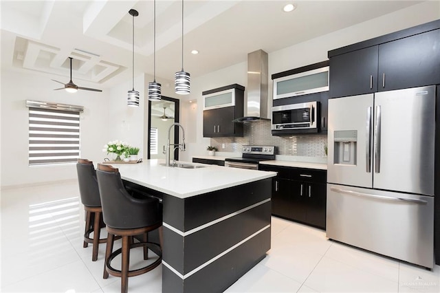 kitchen featuring appliances with stainless steel finishes, decorative light fixtures, sink, a kitchen island with sink, and wall chimney exhaust hood