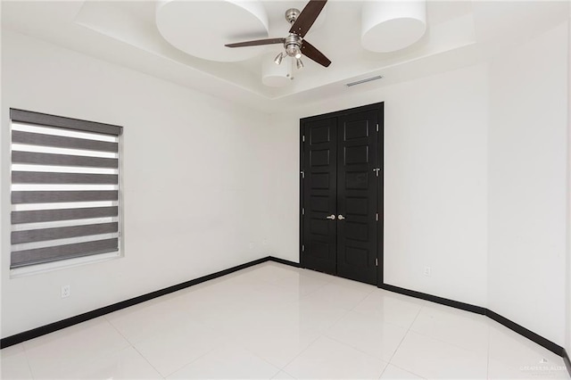 tiled spare room featuring a raised ceiling and ceiling fan