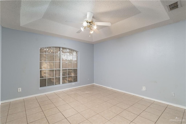 tiled empty room with ceiling fan, a textured ceiling, and a tray ceiling