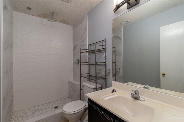 bathroom with a textured ceiling, a tile shower, vanity, and toilet