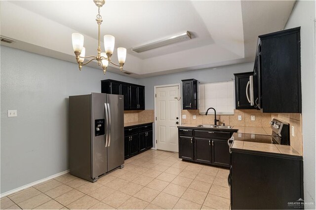 kitchen with stainless steel appliances, a raised ceiling, light tile patterned floors, an inviting chandelier, and sink