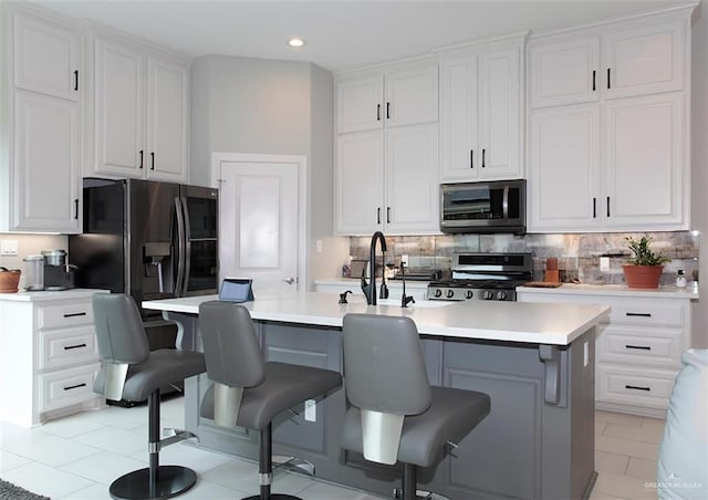 kitchen with white cabinetry, a kitchen breakfast bar, a center island with sink, light tile patterned flooring, and appliances with stainless steel finishes