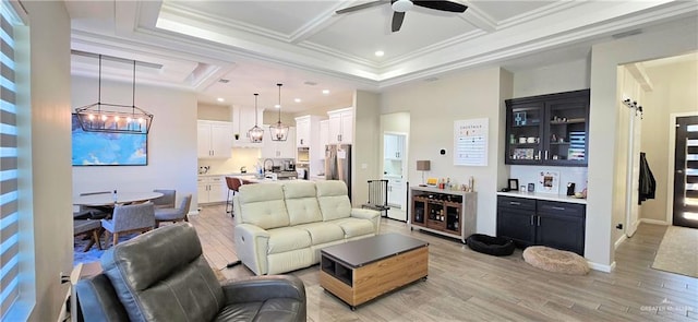 living room featuring crown molding, coffered ceiling, light wood-type flooring, bar, and ceiling fan with notable chandelier