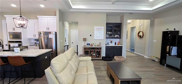 living room with a bar, an inviting chandelier, ornamental molding, and wood finished floors