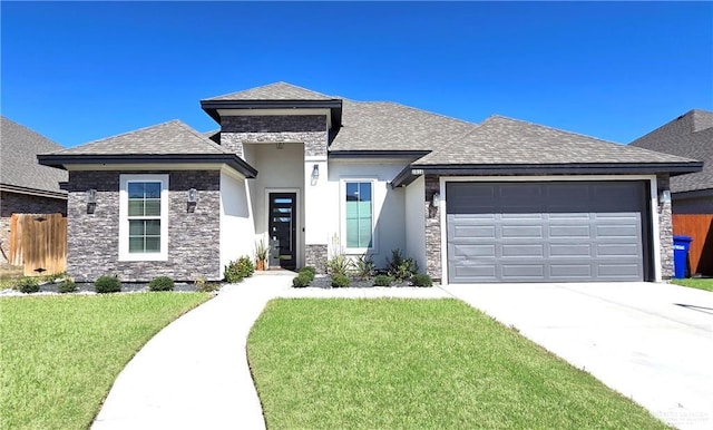 prairie-style home featuring a garage, a shingled roof, concrete driveway, stone siding, and a front lawn