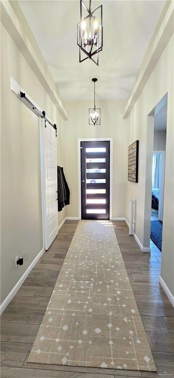 mudroom with dark wood-type flooring, baseboards, an inviting chandelier, and a barn door