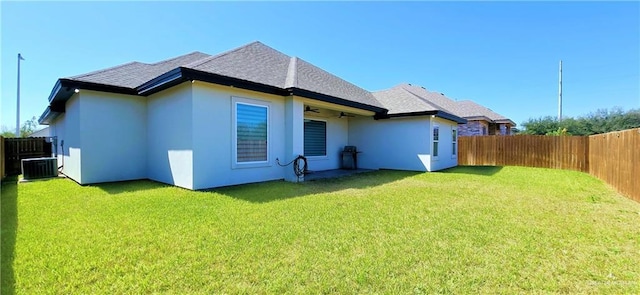 rear view of property with ceiling fan, central AC unit, a lawn, and a fenced backyard