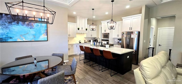 kitchen featuring white cabinets, light countertops, appliances with stainless steel finishes, dark wood-style floors, and a kitchen bar