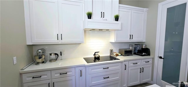 kitchen featuring black electric cooktop, ventilation hood, light countertops, white cabinetry, and backsplash