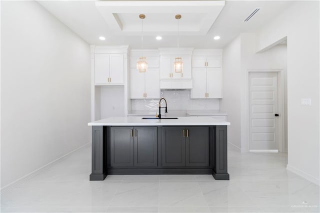 kitchen featuring a raised ceiling, light countertops, a sink, and a kitchen island with sink