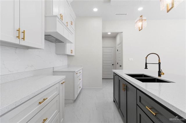 kitchen featuring light stone countertops, white cabinetry, marble finish floor, and a sink