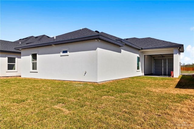 rear view of property with roof with shingles, a yard, and stucco siding