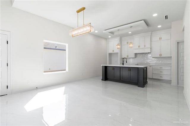 kitchen with a center island with sink, open floor plan, light countertops, white cabinetry, and pendant lighting