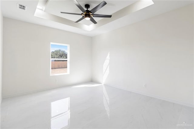 empty room with visible vents, a tray ceiling, ceiling fan, and baseboards