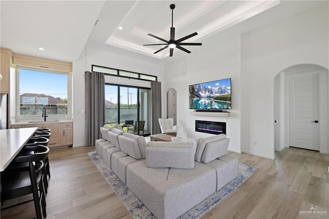5112 W Burberry St, Edinburg, TX 78541 - living room with arched walkways, a tray ceiling, light wood-style floors, a glass covered fireplace, and a towering ceiling