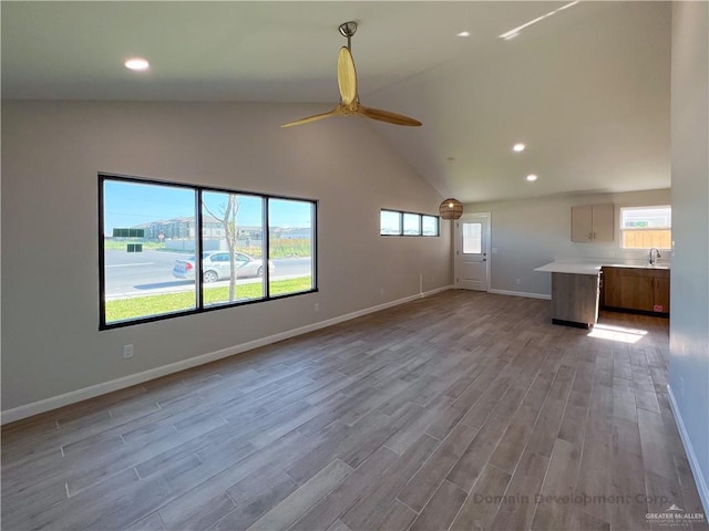 unfurnished living room featuring sink, light hardwood / wood-style flooring, ceiling fan, and vaulted ceiling