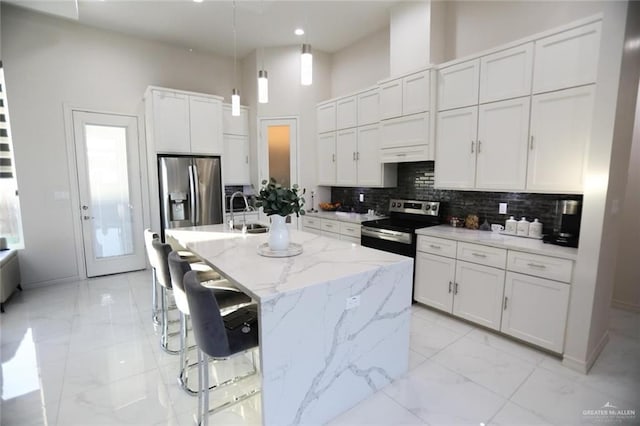 kitchen with an island with sink, a breakfast bar area, appliances with stainless steel finishes, decorative light fixtures, and white cabinets