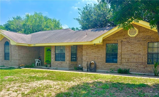 ranch-style home featuring roof with shingles, a front lawn, and brick siding