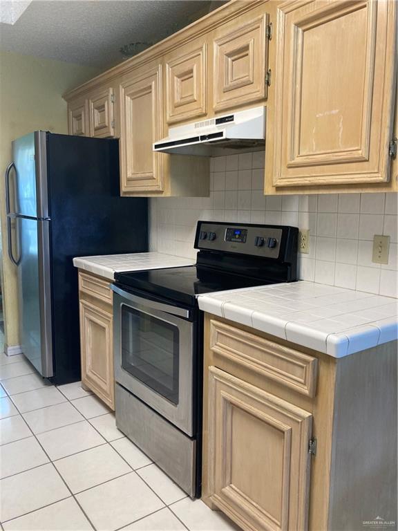 kitchen featuring under cabinet range hood, stainless steel appliances, decorative backsplash, and light tile patterned floors