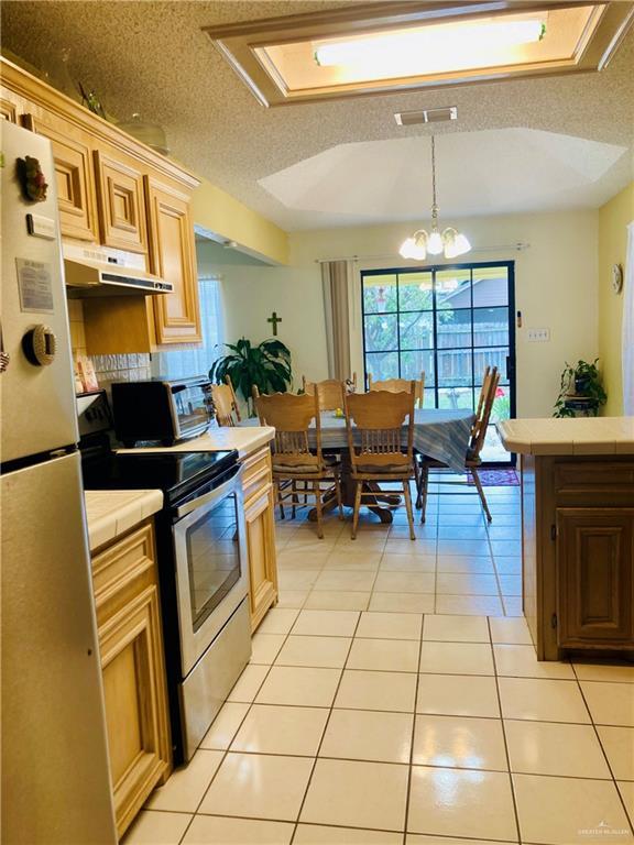 kitchen with tile countertops, visible vents, light tile patterned floors, under cabinet range hood, and stainless steel appliances