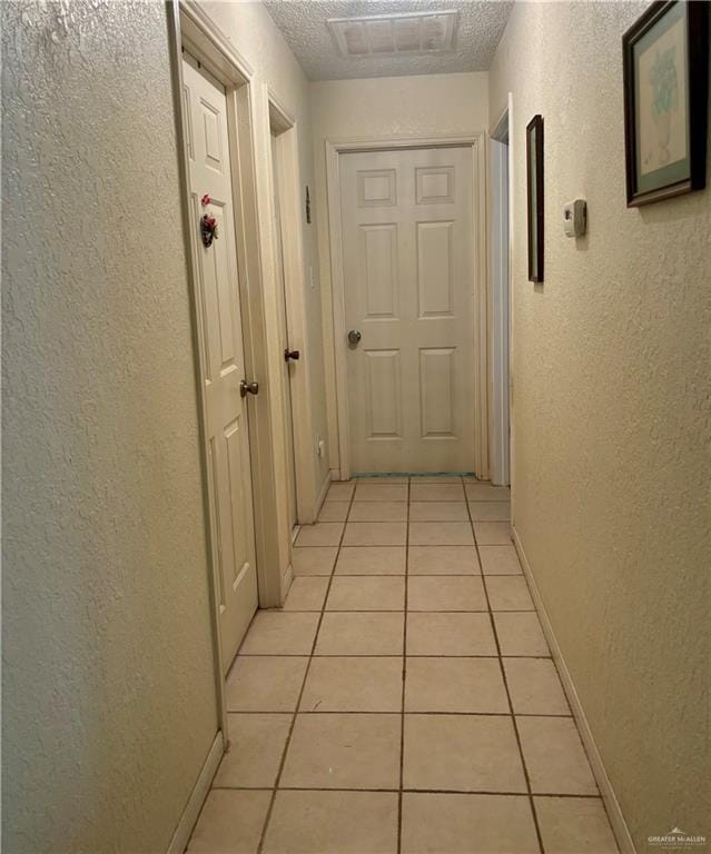corridor featuring visible vents, baseboards, a textured wall, and light tile patterned floors