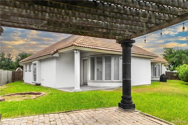 back house at dusk with a yard, a pergola, and a patio area