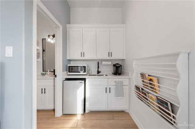 bar featuring refrigerator, white cabinetry, sink, and light hardwood / wood-style flooring