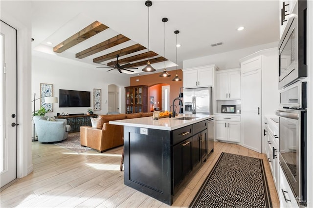 kitchen featuring white cabinets, pendant lighting, a kitchen island with sink, and beamed ceiling